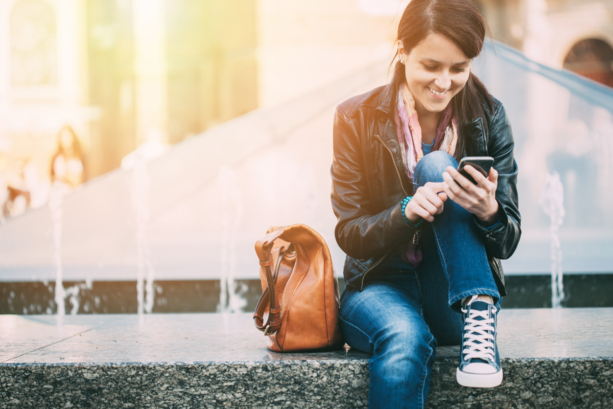 Woman sitting on wall texting and smiling