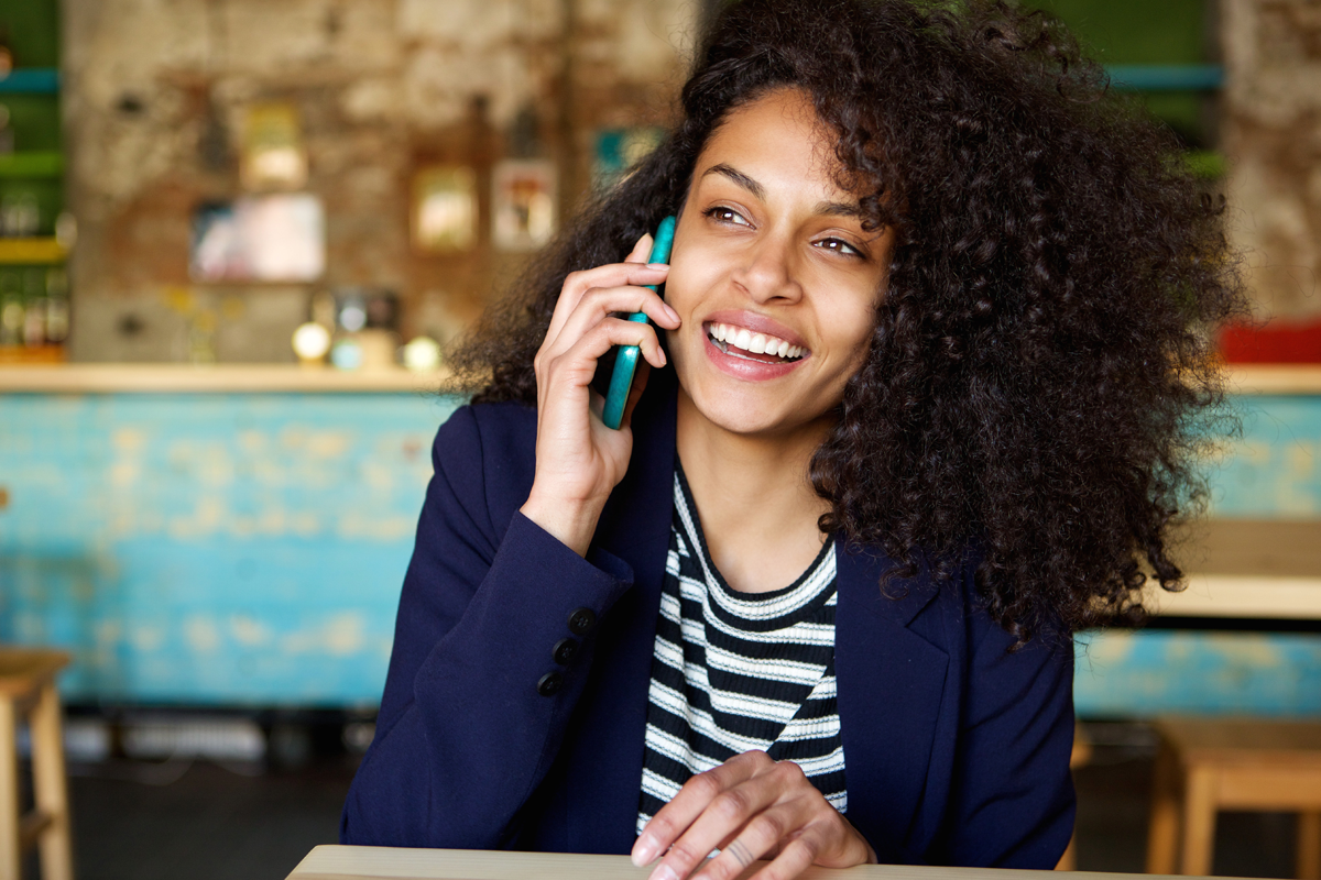 Woman sitting in cafe laughing whilst talking on mobile phone